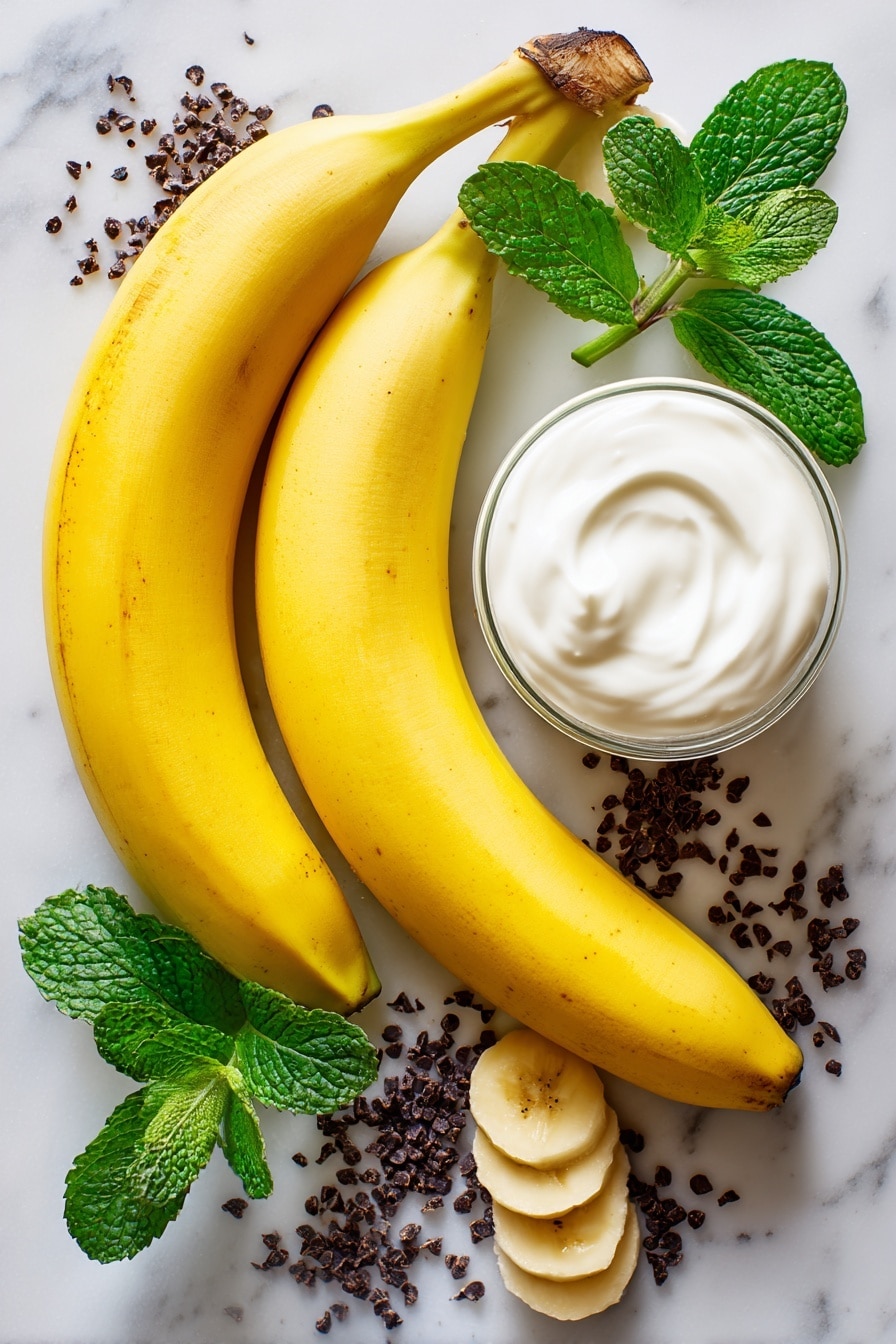 Boonanas – A Frozen Banana Ghost Halloween Treat, Halloween banana treats, healthy Halloween dessert, spooky kid-friendly snacks, frozen banana ghosts - Flat lay of two large ripe bananas with bright yellow skin, a small glass of smooth white vanilla yogurt, and scattered tiny dark mini chocolate chips with a glossy finish, all naturally arranged with a few banana slices showing their creamy texture, some fresh green mint leaves adding a pop of color, placed on white marbled surface, photo taken with an iphone --ar 2:3 --v 7