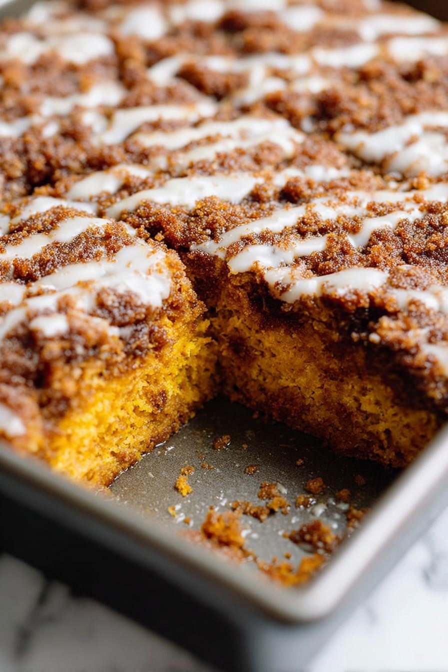 Pumpkin Coffee Cake with Streusel and Glaze, pumpkin coffee cake, fall coffee cakes, pumpkin spice dessert, easy pumpkin cake recipes - A close-up view of a rectangular metal baking pan filled with a baked dish divided into nine square pieces. The top layer is a golden brown crust with a rough, crumbly texture and slight darker spots, suggesting a crispy surface. Beneath the crust, there are hints of a soft, orange layer peeking through in a few spots, showing a moist filling. The pan is placed on a wire rack with a dark surface underneath, creating a rustic feel. photo taken with an iphone --ar 2:3 --v 7