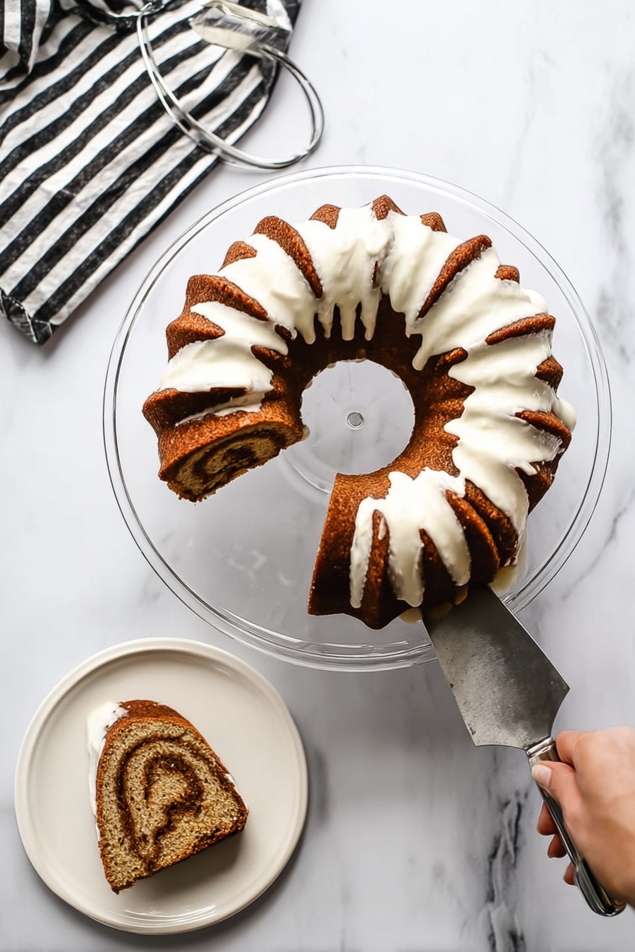 Cinnamon Bundt Cake with Cream Cheese Icing, cinnamon bundt cake recipe, easy cinnamon cake, moist cinnamon cake with cream cheese frosting, homemade cinnamon bundt cake - A bundt cake with a rich brown color and a thick white icing drizzled over the top that flows down the sides, leaving some of the cake visible between the icing sections. The cake is placed on a clear glass pedestal plate on a white marbled surface. One slice is cut out and placed on a white plate nearby, showing a swirl pattern inside with light and dark brown layers. A woman's hand is holding the cake server that has been used to lift the slice from the bundt cake. There is a striped black and white napkin to the side with a metal cake server on it. photo taken with an iphone --ar 2:3 --v 7