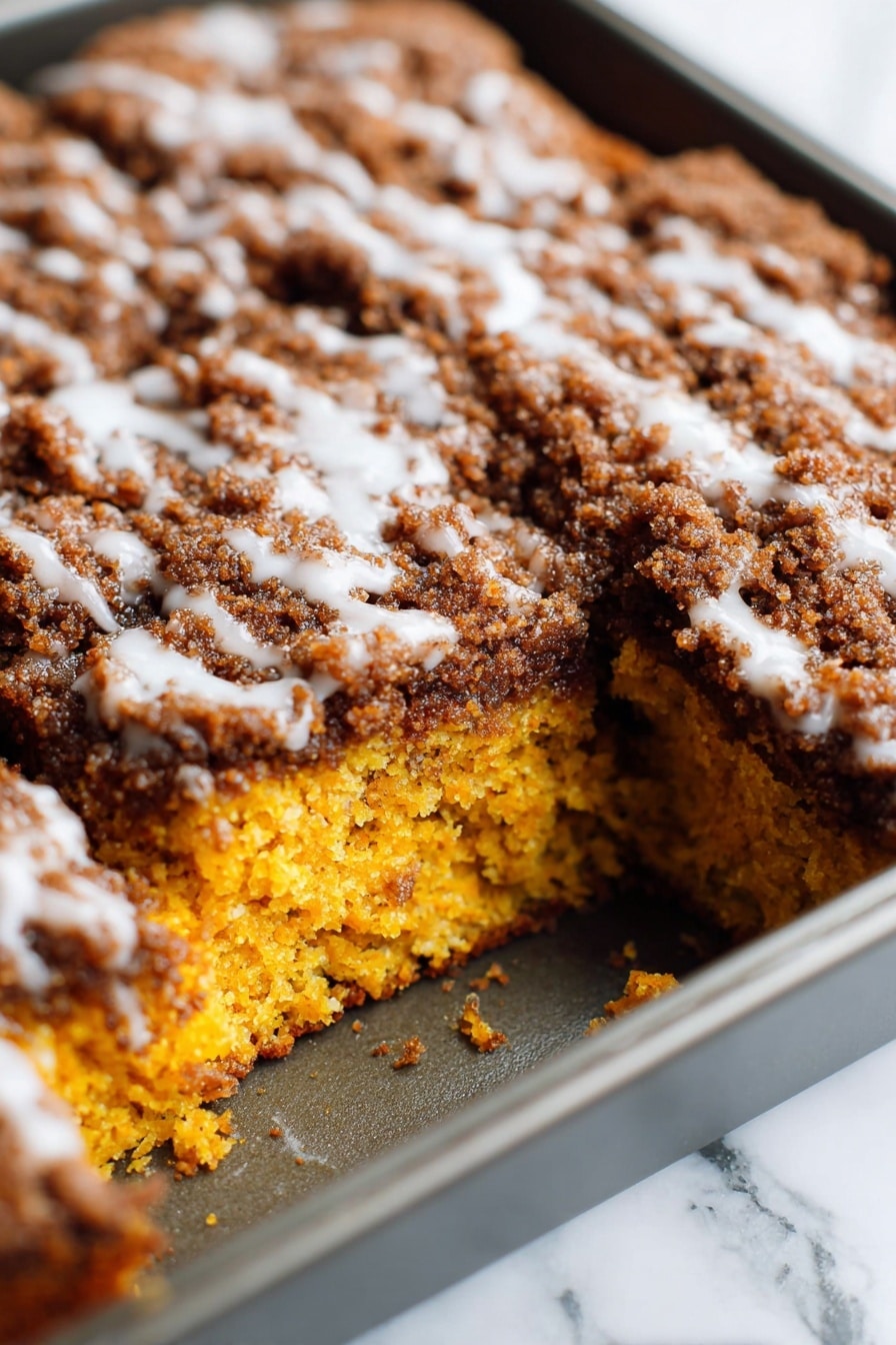 Pumpkin Coffee Cake with Streusel and Glaze, pumpkin coffee cake, fall coffee cakes, pumpkin spice dessert, easy pumpkin cake recipes - A close-up view of a square cake in a baking pan, showing one large piece missing from the corner of the cake. The cake has two visible layers: the bottom layer is bright orange with a moist and soft texture, and the top layer is thick with a dark brown crumbly topping mixed with a white glaze lightly drizzled over it. The baking pan is metallic, and the background surface is a white marbled texture. photo taken with an iphone --ar 2:3 --v 7