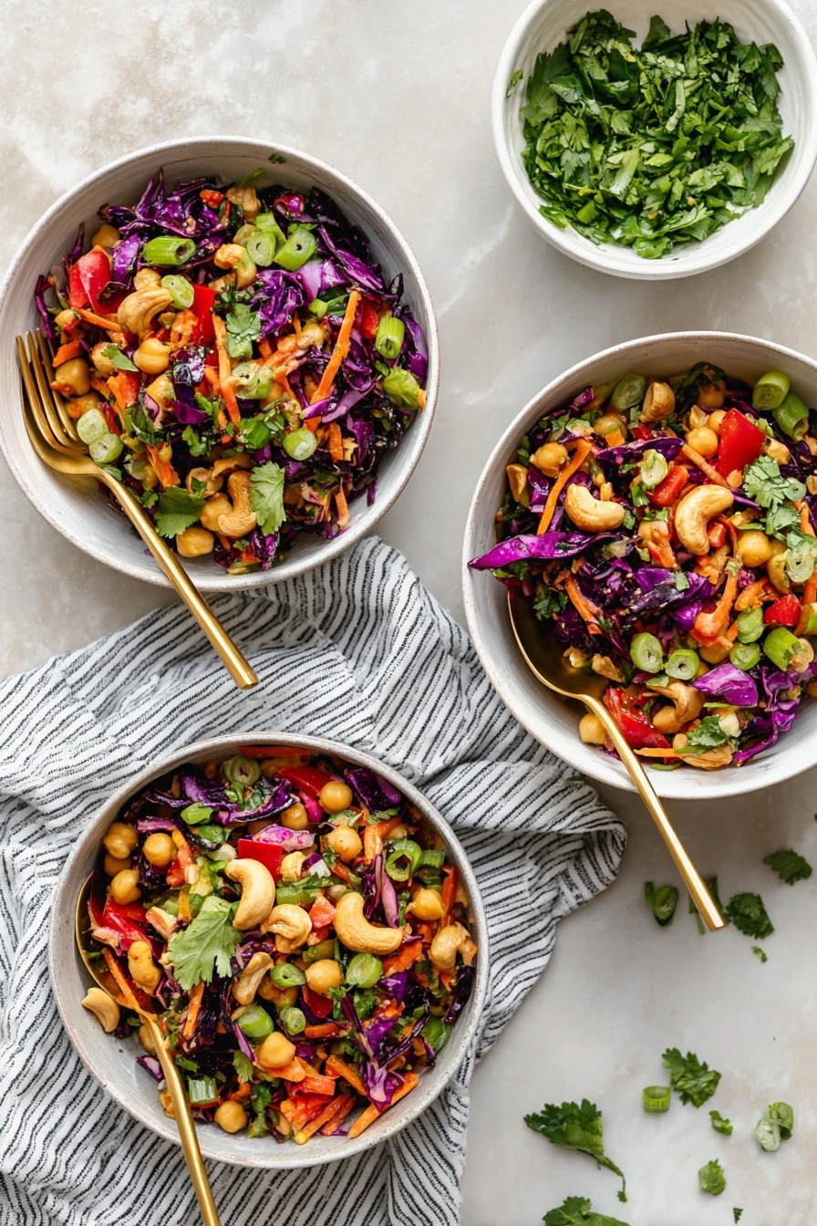 Chopped Thai-Inspired Chickpea Salad with Curry Peanut Dressing, Thai chickpea salad, healthy chickpea salad recipe, vegan Thai salad, quick Asian chickpea salad - Three white bowls filled with a colorful salad sit on a white marbled texture. Each bowl holds a mix of dark purple cabbage pieces, orange shredded carrots, light yellow chickpeas, green sliced scallions, red bell pepper chunks, and fresh green cilantro leaves scattered on top. There are some whole cashews on the salad adding a light beige color. Each bowl has a gold spoon resting inside, and a striped white and navy cloth lies underneath two of the bowls. A small white bowl with chopped cilantro sits above the bowls, with some cilantro leaves scattered on the surface. photo taken with an iphone --ar 2:3 --v 7