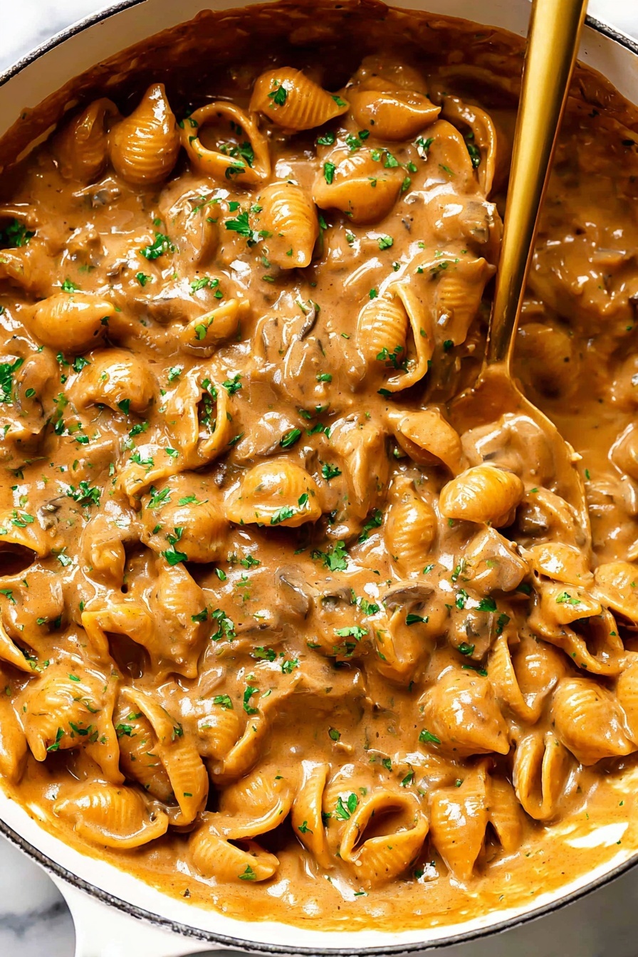 French Onion Pasta with Gruyere, French onion pasta, caramelized onion pasta, cheesy pasta recipes, easy French onion pasta - A close-up view of a white pan filled with a rich, creamy mushroom sauce that has a warm brown color and a thick texture. The sauce contains many small mushroom slices that create a bumpy surface, covered evenly in the glossy, smooth sauce. Bright green parsley bits are scattered on top, adding a touch of color contrast. A shiny golden spoon rests inside the pan, partially submerged in the sauce, showing the thick consistency as it drags some sauce along. The background features a white marbled surface. photo taken with an iphone --ar 2:3 --v 7