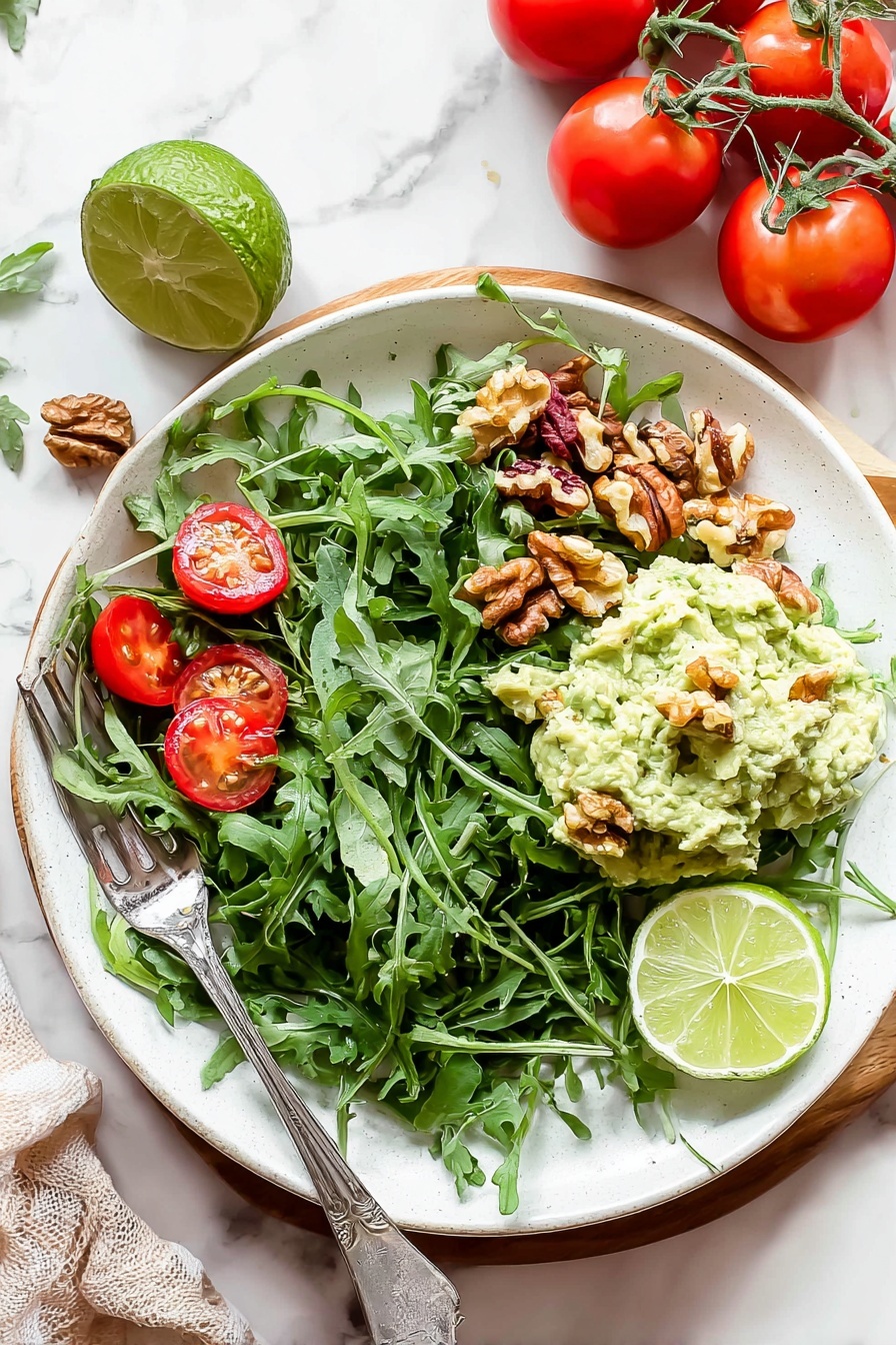 Healthy Greek Yogurt Avocado Chicken Salad, healthy chicken salad, avocado chicken salad, Greek yogurt chicken salad, gluten-free chicken salad - A white plate filled with a fresh salad on a white marbled surface. The bottom layer is a bed of dark green arugula leaves spread across the plate. Scattered on top are bright red cherry tomato halves and small brown walnut pieces. On one side, a creamy pale green mashed avocado mix is placed in a mound with a few walnut pieces on it. Two lime wedges, one light green and one yellow-green, rest on the mashed avocado. A silver fork is placed on the left side of the plate, partially resting on the salad. Nearby, whole red tomatoes on the vine and a halved lime sit on the white marbled background. Photo taken with an iphone --ar 2:3 --v 7