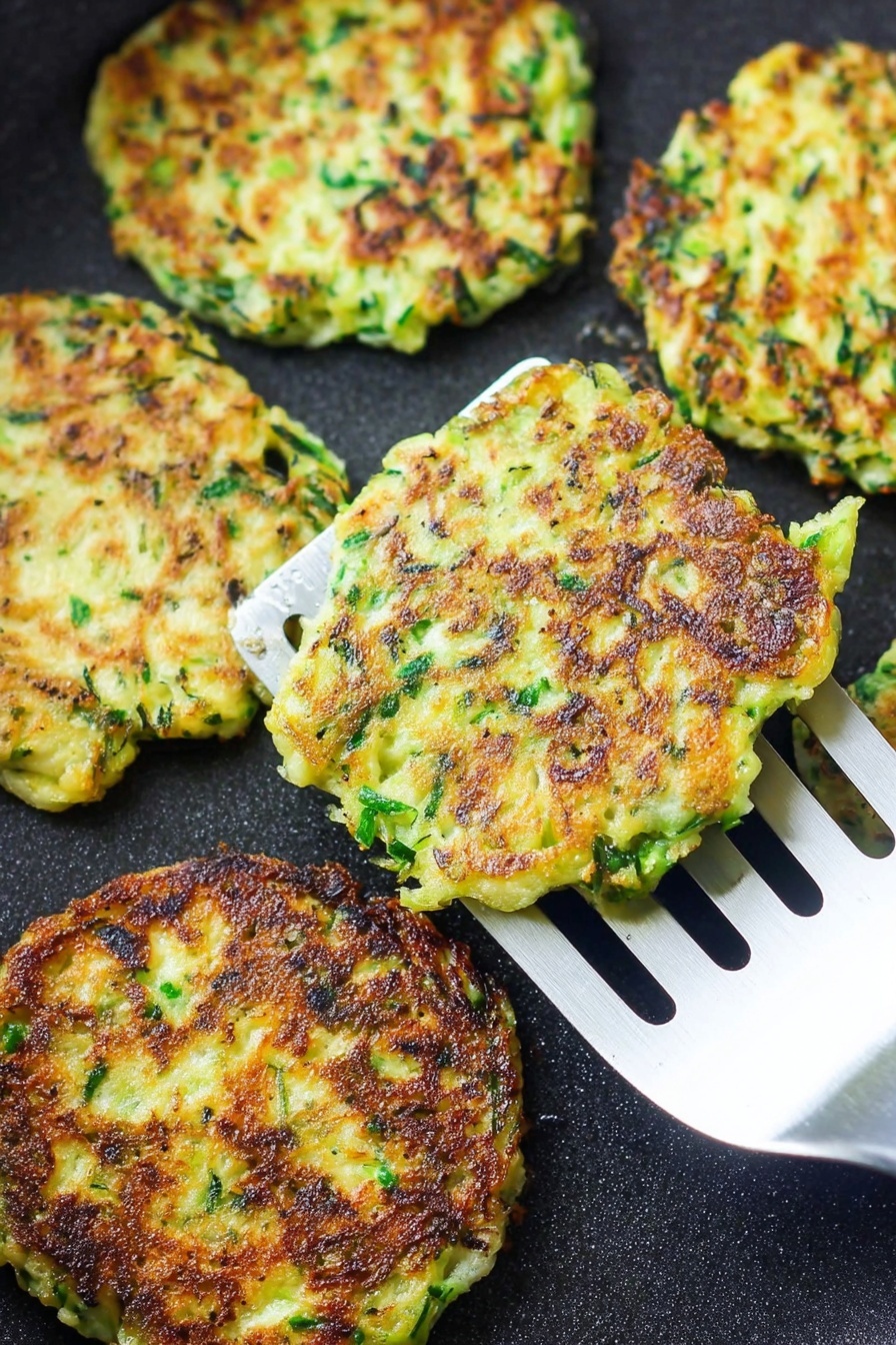 Vegan Zucchini Fritters, vegan vegetable fritters, healthy zucchini snacks, crispy vegan fritters, quick vegan meal - There are several flat, round fritters cooking on a black pan. Each fritter shows a mix of green herbs and light yellow batter, with crisp, dark brown patches where they have browned. One fritter is lifted by a silver spatula with long slots, showing its uneven edges and slightly rough texture. The overall look is crispy and fresh, with the green and yellow colors standing out against the pan. photo taken with an iphone --ar 2:3 --v 7