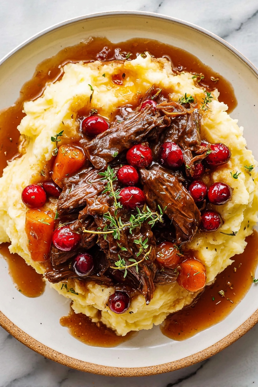 Cranberry Balsamic Roast Beef, roast beef with cranberries and balsamic, festive beef roast recipe, easy holiday roast beef, tender roast beef for dinner - A white plate holds a large bed of soft, creamy mashed potatoes that have a smooth, slightly lumpy texture and a pale yellow color. On top, there are several pieces of dark brown shredded beef covered in a glossy, thick brown gravy with visible chunks of carrots, pearl onions, and whole bright red cranberries scattered throughout. Fresh small green herb leaves, possibly thyme, are sprinkled over the dish. Some gravy has spilled onto the plate, adding a rich shine. The plate sits on a white marbled surface. Photo taken with an iphone --ar 2:3 --v 7