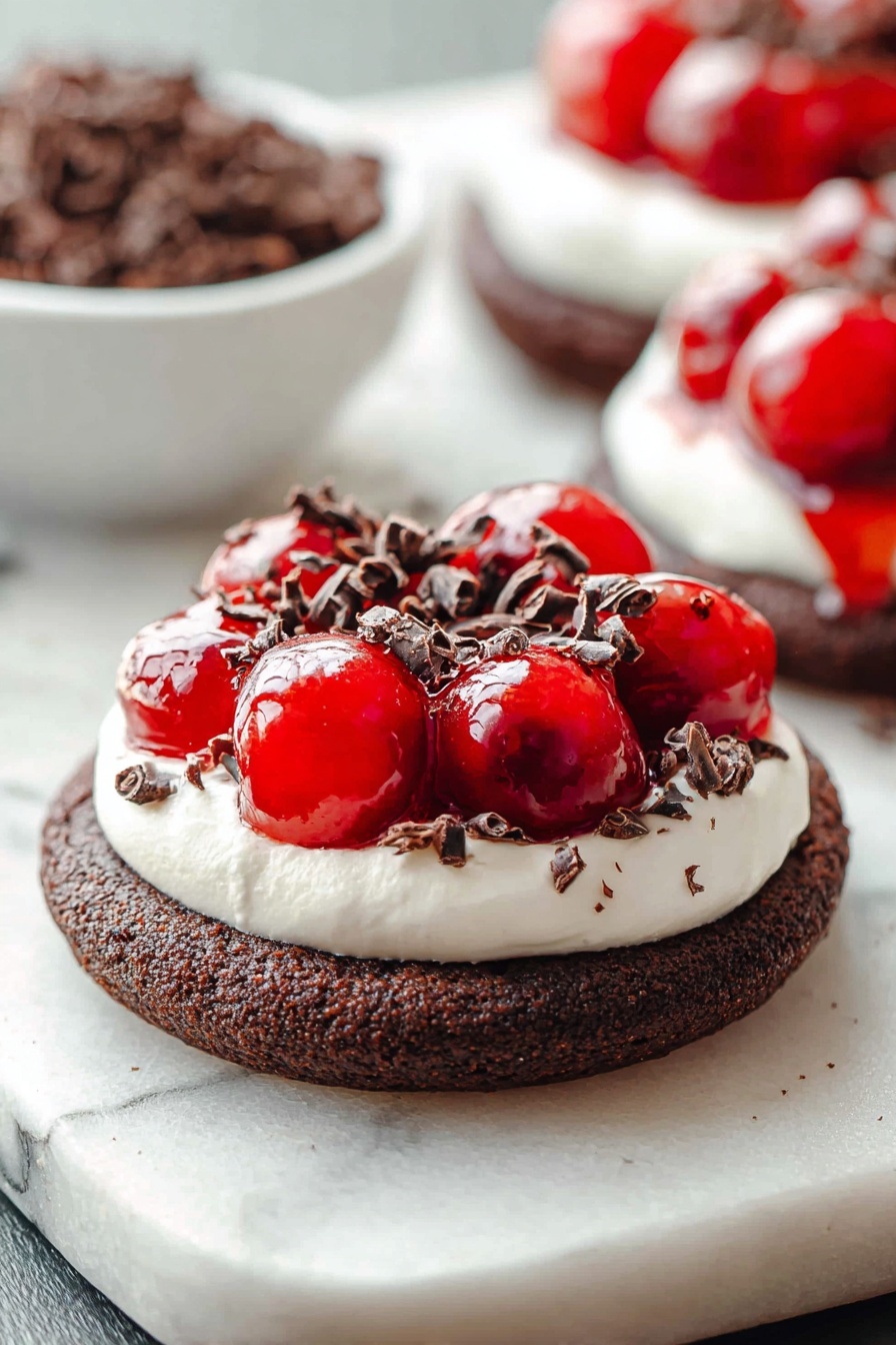 Chocolate Cherry Cheesecake Cookies, cherry chocolate cookie recipe, no-bake cheesecake cookies, easy fruit dessert cookies, chocolate cherry dessert - The image shows a dessert with three layers on a white marbled surface. The bottom layer is a thick, round dark brown chocolate cookie with a coarse texture. The middle layer is a white creamy topping, spread evenly in a smooth circle covering the cookie’s surface. On top, there is a shiny bright red cherry topping that looks wet and glossy, with whole cherries visible. Small dark brown curled chocolate pieces are sprinkled over the cherry topping and creamy layer, adding texture and contrast. In the background, a white bowl filled with more dark brown chocolate curls is blurred, along with a second dessert of the same kind slightly out of focus. photo taken with an iphone --ar 2:3 --v 7