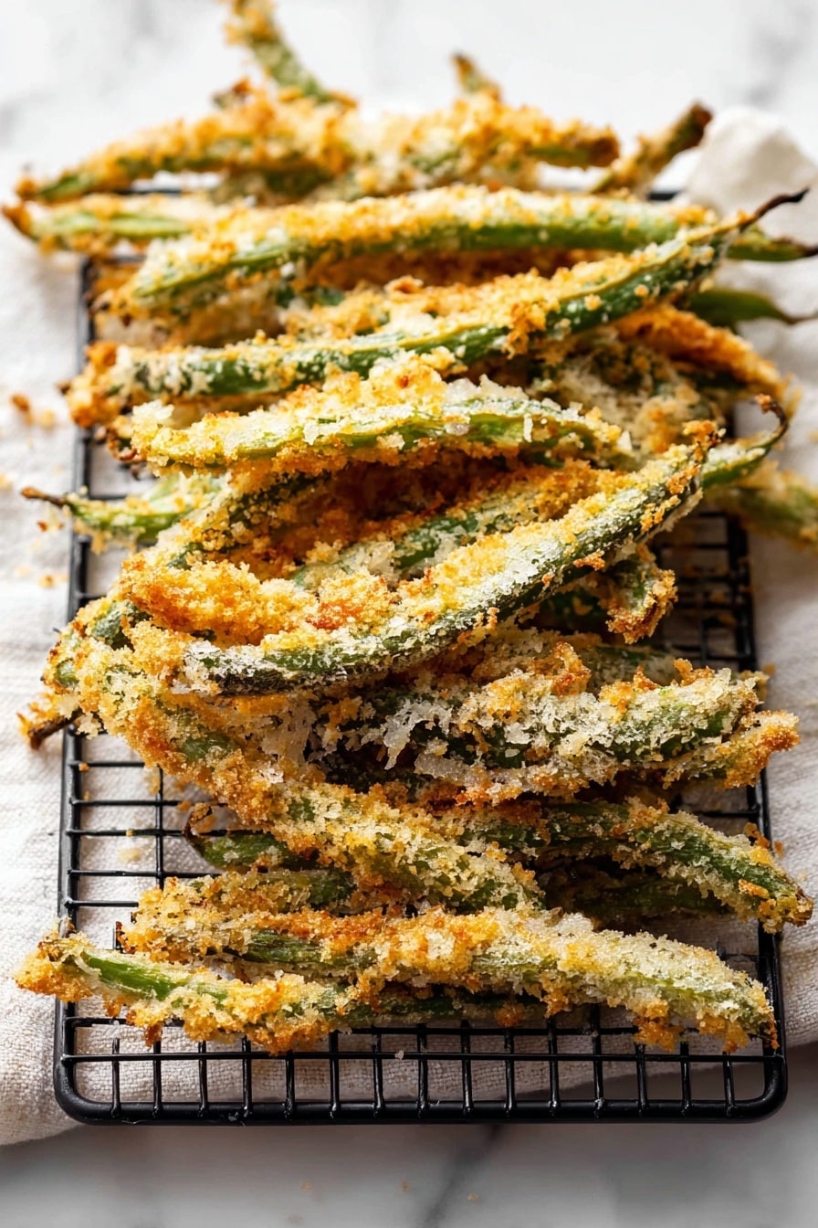 Green Bean Fries, crispy green bean snack, baked green bean appetizer, healthy green bean recipe, crunchy green bean sticks - The image shows a stack of crispy baked green beans coated with a light golden-brown breadcrumb crust. The green beans are arranged in a slightly overlapping pile on a black wire rack that sits on top of a white marbled surface with a soft white cloth underneath. The crumb coating is uneven with some areas showing more toasted crispiness and a mix of pale and deeper golden colors. The green beans are long and thin, with their stems visible at the edges, and the texture looks crunchy and rustic. photo taken with an iphone --ar 2:3 --v 7
