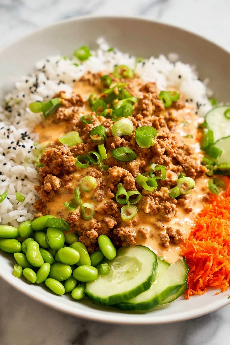 Ground Turkey Rice Bowls with Bang Bang Sauce, ground turkey rice bowls, spicy turkey rice bowl, quick dinner recipes, easy weeknight meals - A white plate holds a colorful, layered meal starting with a base of white rice scattered with small black seeds. On top of the rice, there is a generous layer of brown ground meat covered in a creamy, light orange sauce. Bright green sliced scallions are sprinkled over the meat and sauce. Around the main layers are small piles of bright green edamame, thin slices of cucumber, and grated orange carrots, all sitting on a white marbled surface. Photo taken with an iphone --ar 2:3 --v 7
