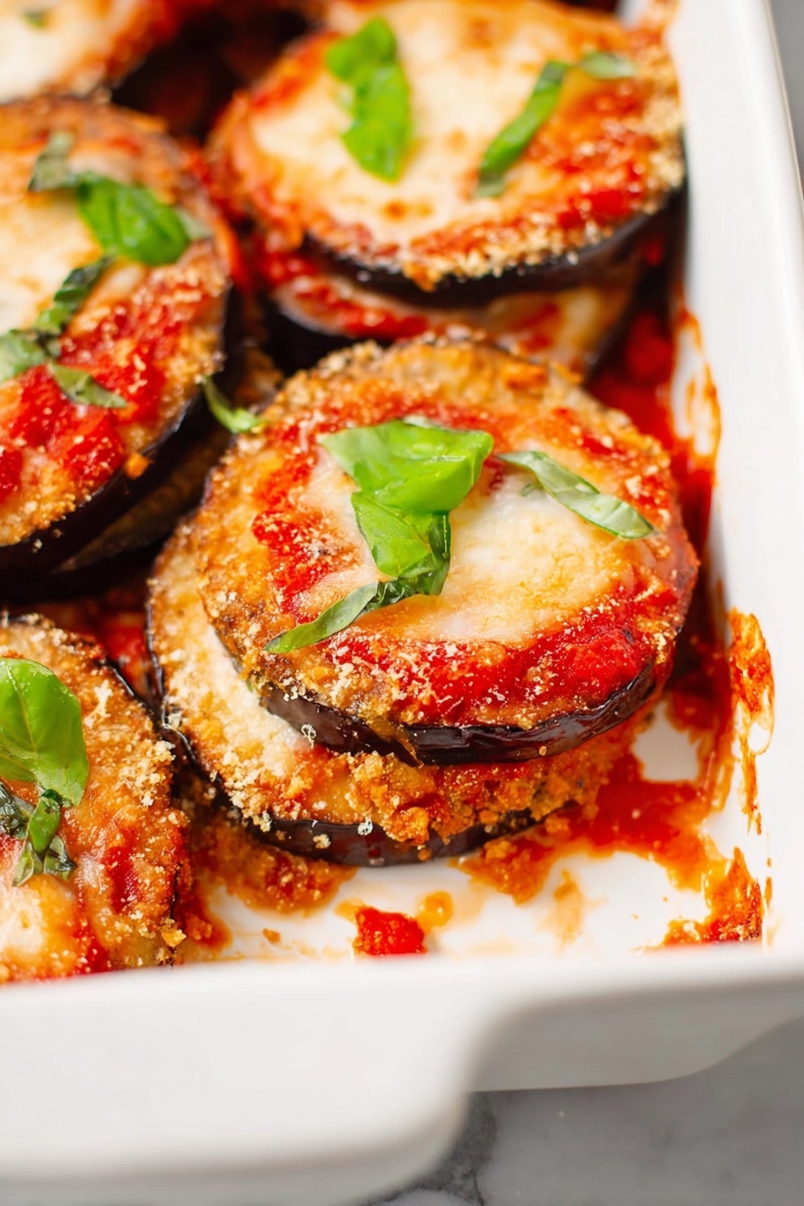 Vegan Eggplant Parmesan, vegan eggplant parmesan recipe, plant-based eggplant parmesan, healthy vegan eggplant dish, dairy-free eggplant parmesan - The image shows a white ceramic baking dish filled with several layered stacks of eggplant Parmesan. Each stack has a bottom layer of crispy, golden-brown eggplant slices with a rough texture, topped with rich red tomato sauce, then a layer of melted pale orange cheese that is slightly bubbly and browned in spots. Bright green basil leaves are scattered on top of the stacks and around the dish for color contrast. There are some tomato sauce spills and melted cheese crumbs inside the dish on a white marbled surface. Photo taken with an iphone --ar 2:3 --v 7