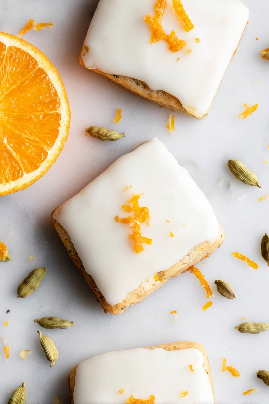 Cardamom Shortbread Cookies with Orange Glaze, aromatic shortbread cookies, orange glazed shortbread, festive holiday cookies, buttery spice cookies - The image shows three square-shaped cookies with smooth white icing covering the top layer. Each cookie is slightly thick, with the base layer visible under the icing, showing a light golden-brown color and a slightly textured edge. Small pieces of orange zest are scattered on top of the icing, adding a bright orange color contrast. To the left side of the cookies, there is a fresh orange half with a vibrant, juicy orange color. Around the cookies on the white marbled surface, there are several light green cardamom pods and scattered bits of orange zest. The photo taken with an iphone --ar 2:3 --v 7