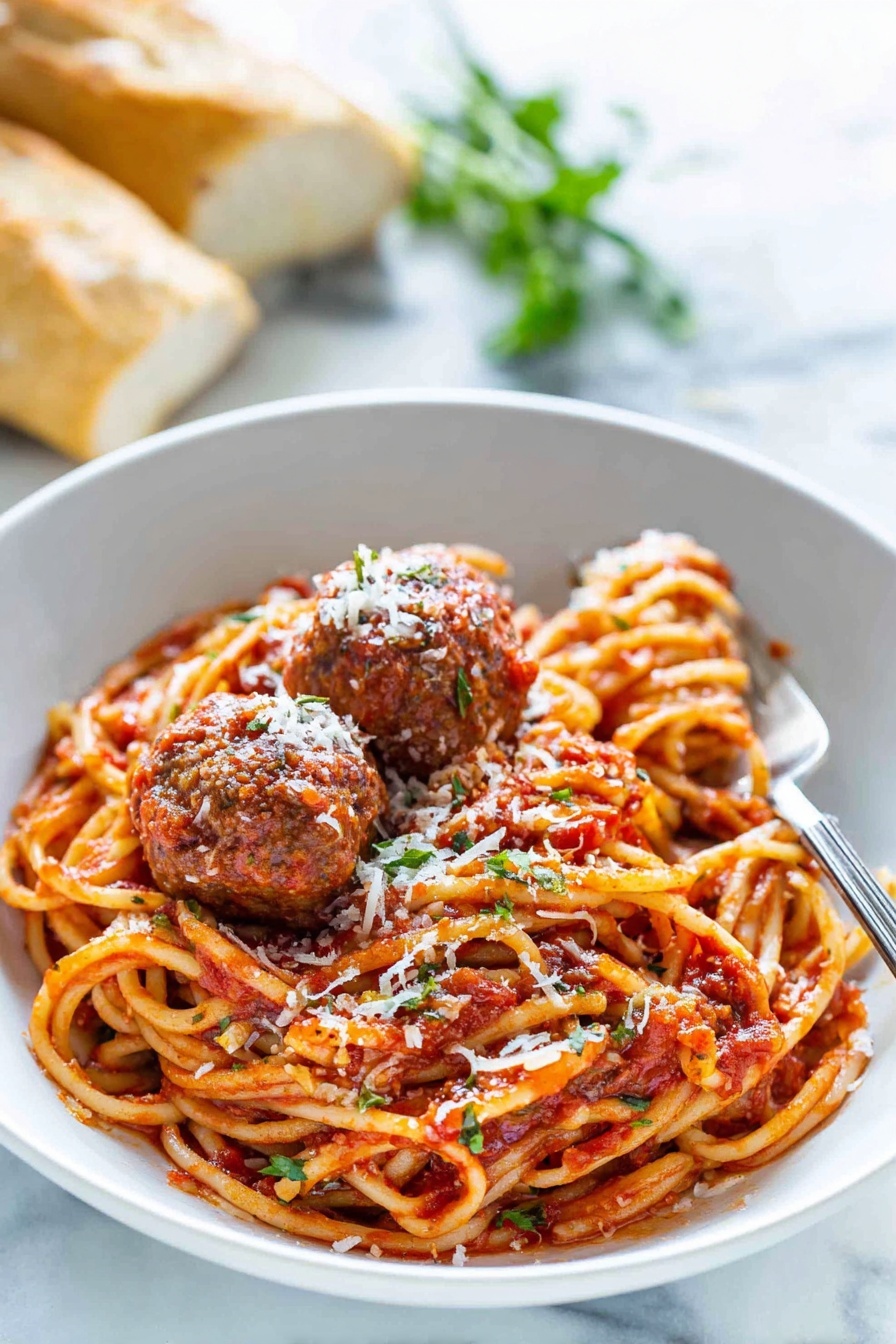 Spaghetti and Meatballs, easy spaghetti and meatballs, homemade meatballs, quick Italian dinner, comforting pasta recipe - A white bowl holds a serving of spaghetti noodles mixed with red tomato sauce, showing some herbs and seasoning. On top, there are three brown meatballs covered in sauce and sprinkled with white grated cheese. A silver fork rests inside the bowl on the right side. In the background, there is a blurred fresh green herb and some pieces of bread. The bowl sits on a white marbled surface. photo taken with an iphone --ar 2:3 --v 7