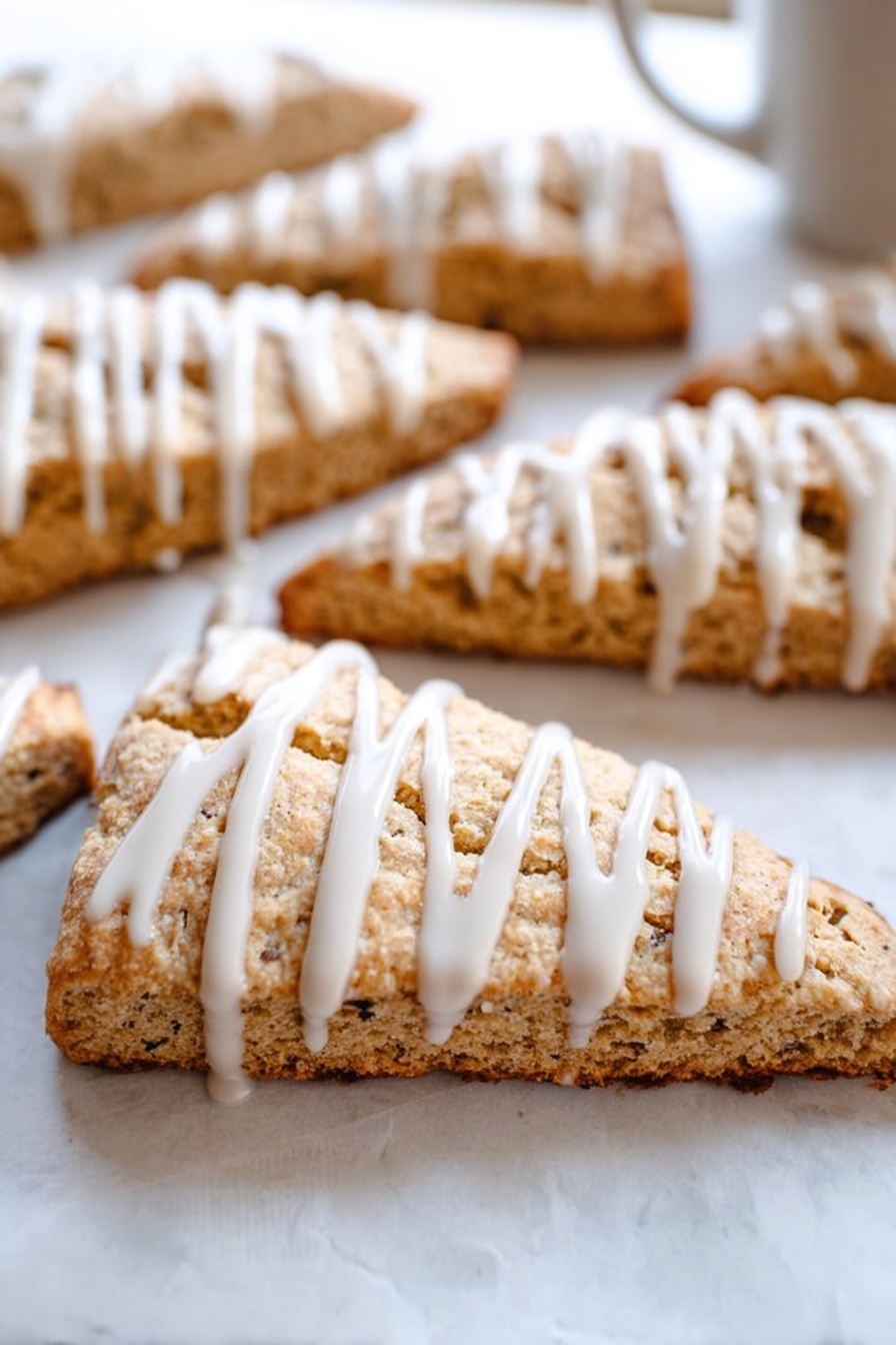 Cinnamon Vanilla Biscotti, best biscotti recipe, crunchy biscotti with cinnamon, homemade vanilla biscotti, coffee pairing biscotti - This image shows several triangular slices of light brown scones arranged on white parchment paper over a white marbled surface. Each scone slice has a visible crumbly texture with small dark specks inside. On top of each slice, there is a thick white icing drizzle applied in vertical lines, adding contrast and a smooth, glossy look to the rough texture of the scones. The focus is on a front scone slice, with others blurred in the background, giving depth to the image. photo taken with an iphone --ar 2:3 --v 7