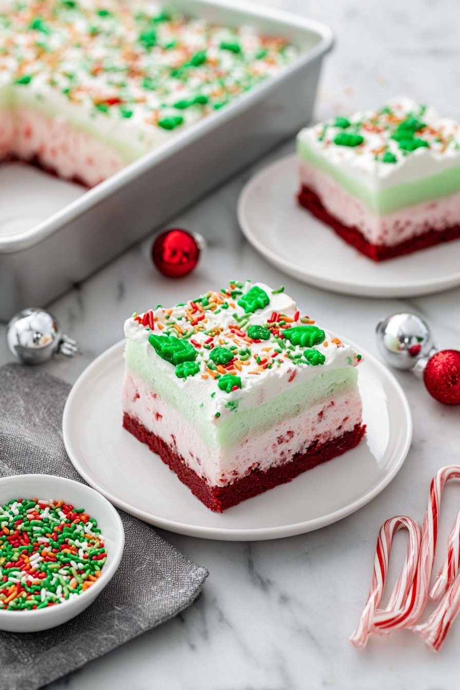 Christmas Red Velvet Lasagna Dessert, festive red velvet dessert, holiday layered dessert, Christmas holiday dessert ideas, easy Christmas dessert recipes - The image shows a festive layered dessert square on a white plate, placed on a white marbled surface. The dessert has four distinct layers: the bottom layer is a dense dark red cake, followed by a light pink creamy layer with red specks, then a smooth pale green gelatin layer, and finally topped with a thick white whipped cream layer decorated with green, red, orange, and white sprinkles shaped like leaves, dots, and sticks. In the background, there is a silver baking pan with a large portion of the same dessert topped with sprinkles, and another smaller white plate holds a similarly decorated dessert square. Nearby, a small white bowl filled with matching festive green and red sprinkles sits next to two small candy canes, a silver ornament ball, a red ornament ball, and a gray cloth napkin. Photo taken with an iphone --ar 2:3 --v 7