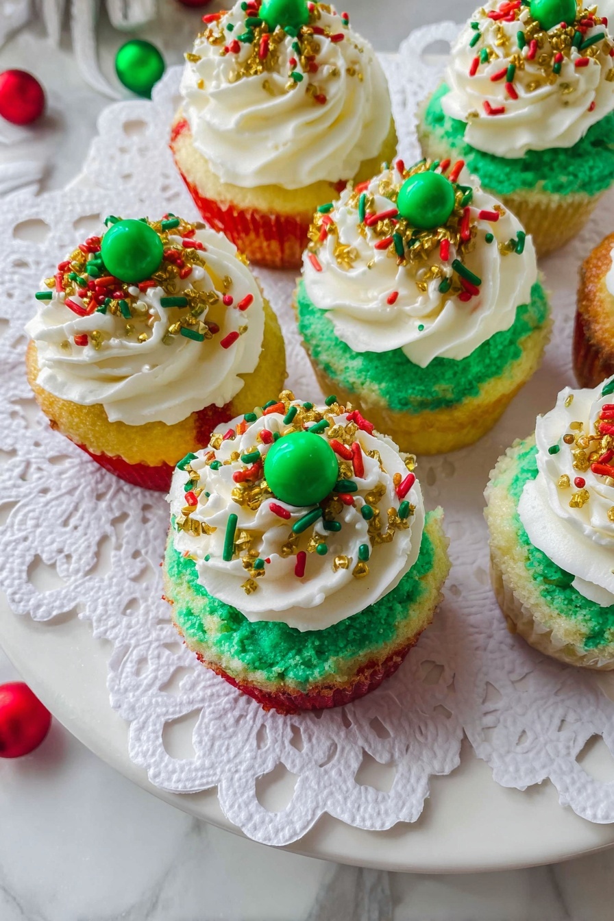Mini Christmas Cheesecake Bites, festive cheesecake desserts, holiday mini cheesecakes, Christmas party dessert bites, easy holiday cheesecake treats - The image shows six cupcakes placed on a white plate covered with a white paper doily. Each cupcake has three visible layers of cake with red, yellow, and green colors, stacked one on top of another. On top of the cake layers is a thick layer of green frosting spread evenly. Over this green frosting, there is a generous swirl of white whipped cream. The whipped cream is decorated with holiday-themed sprinkles in red, green, and gold, including small rods, round dots, and tiny gold balls. Two cupcakes have a green candy ball placed in the center on top of the whipped cream. The plate is set on a white marbled surface with some colorful decorations partially visible around the edges. photo taken with an iphone --ar 2:3 --v 7