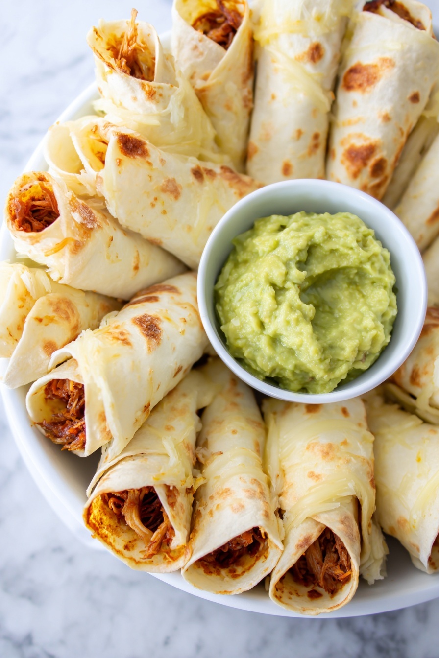 Cheesy Chicken Burrito Ring, cheesy chicken burrito ring, chicken burrito ring recipe, easy burrito ring, cheesy appetizer ideas - A round white plate holds a circle of rolled tortilla cones filled with a reddish-orange shredded filling, each cone standing upright and leaning slightly outward. The tortillas are lightly toasted with brown spots and some melted cheese visible near the edges. In the center of the plate, there is a small white bowl filled with smooth light green guacamole. The plate is set on a white marbled surface. Photo taken with an iphone --ar 2:3 --v 7