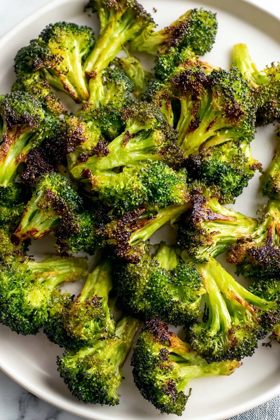 Oven Roasted Broccoli with Spices, roasted broccoli side dish, spicy broccoli recipe, garlic paprika broccoli, healthy roasted vegetable - A white round plate is filled with many pieces of roasted broccoli. Each broccoli piece shows a bright green color with dark brown, crispy edges where it is roasted. The broccoli is scattered all over the plate, with some pieces standing up and others lying flat, showing their textured tops and thick stalks. The plate is placed on a white marbled surface. photo taken with an iphone --ar 2:3 --v 7