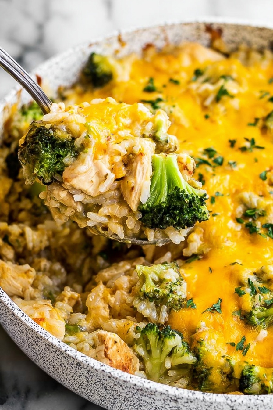 Cheesy Chicken Broccoli Rice Casserole, chicken broccoli rice bake, cheesy chicken casserole, easy chicken and rice dinner, hearty broccoli casserole - The image shows a close-up of a dish in a white speckled pan filled with a cheesy mixture. The dish has two main layers: at the bottom, tender pieces of light brown chicken mixed with white rice; on top, bright green broccoli florets are scattered evenly. A thick layer of melted yellow cheese covers the whole dish, with some green herbs sprinkled on top. A metal spoon lifts a portion, showing the mix of chicken, rice, broccoli, and cheese together. The background is a white marbled texture. Photo taken with an iphone --ar 2:3 --v 7