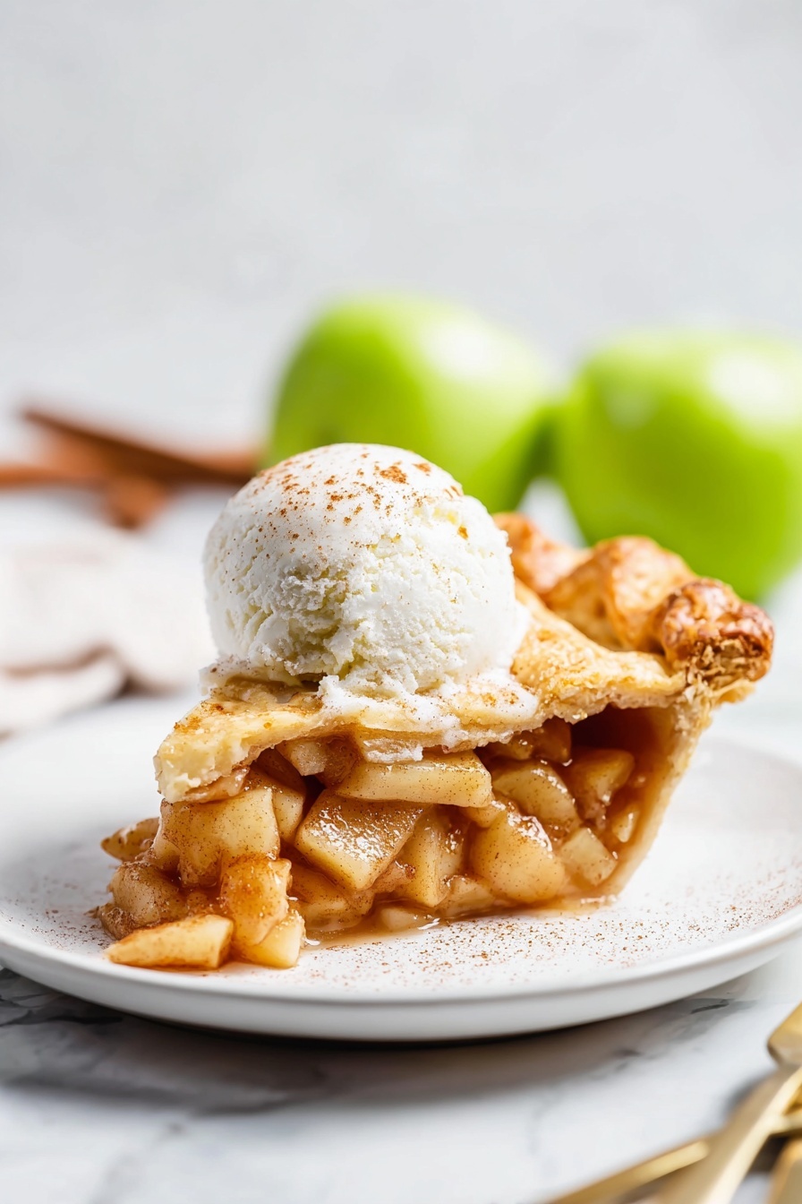 Vegan Pear Pie with Chai Spices, vegan pear pie, chai spice dessert, vegan fruit pie, fall vegan dessert - A slice of apple pie sits on a white plate, showing three main layers: the bottom crust is golden brown and slightly flaky, the middle layer is filled with soft, cinnamon-spiced apple pieces that look juicy and tender, and the top crust is also golden with a slight sprinkle of sugar. On top of the pie slice is a round scoop of white ice cream with a light dusting of cinnamon. The plate rests on a white marbled surface, and in the background, out of focus, two green apples and a fork and knife are visible. Photo taken with an iphone --ar 2:3 --v 7