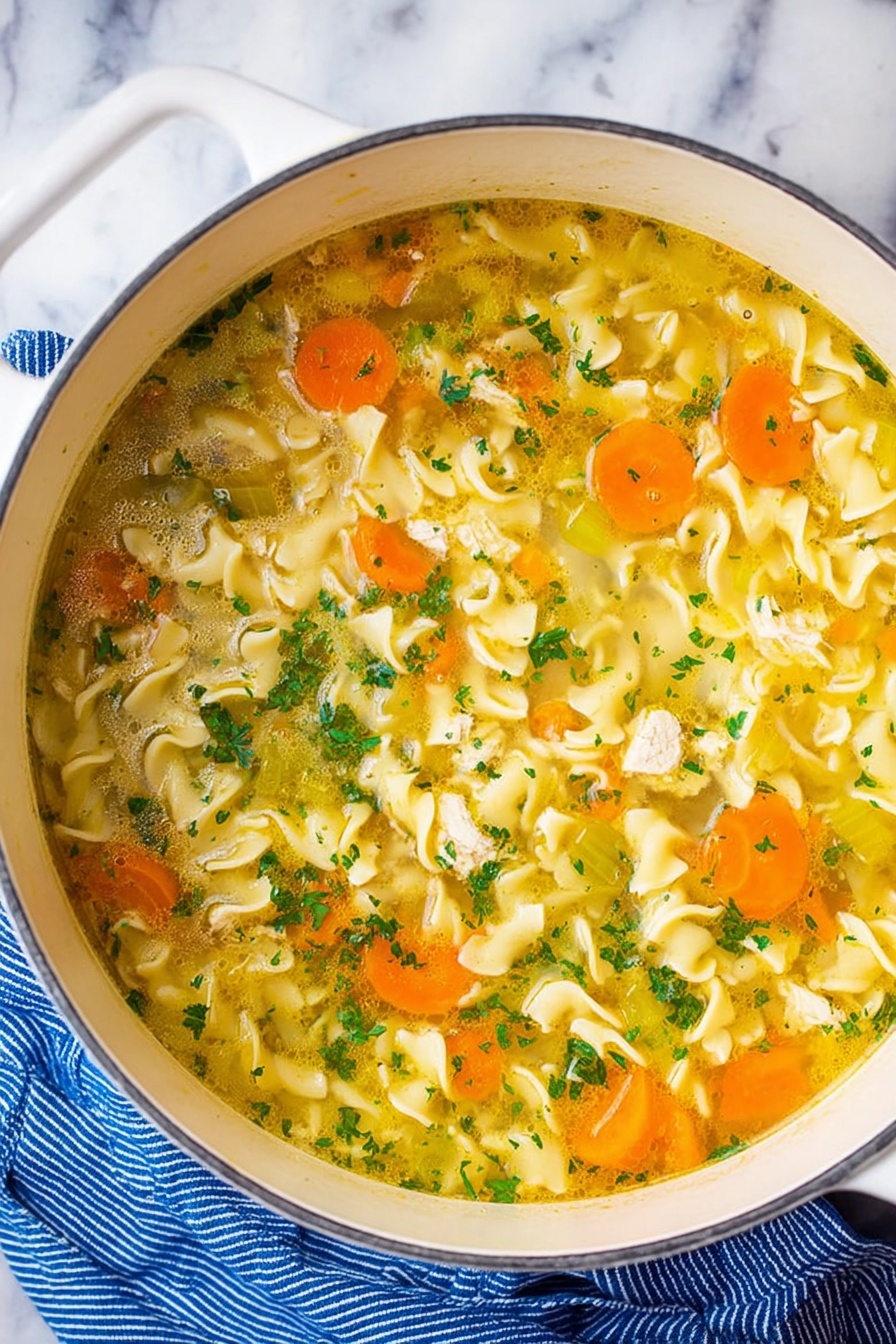 Vegan Chicken Noodle Soup, plant-based chicken noodle soup, vegan comfort food recipes, dairy-free chicken noodle soup, healthy vegan soup recipes - A white pot filled with clear yellow broth soup containing wavy egg noodles that float through the liquid. Slices of bright orange carrots and pale green celery are mixed evenly throughout the soup, along with small pieces of white chicken. The soup is topped with finely chopped fresh green herbs, adding small bursts of color. The pot is resting on a white marbled surface next to a blue striped cloth. Photo taken with an iphone --ar 2:3 --v 7