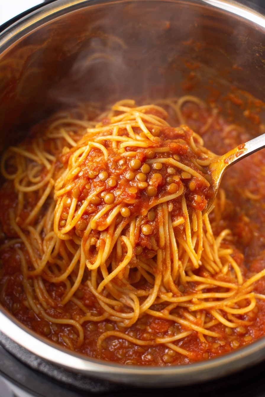 Instant Pot Lentil Spaghetti, Lentil Spaghetti Recipe, Healthy Lentil Pasta, Easy Instant Pot Dinner, Protein-Packed Pasta Dish - A close-up view inside a shiny stainless steel pot filled with spaghetti noodles mixed with small lentils in a rich red tomato sauce; the noodles have a soft yellow color and are coated well by the thick, slightly chunky sauce; a spoon is stirring the mixture, showing a tangled clump of noodles lifted above the rest with pieces of lentils visible around; steam rises gently from the hot dish. photo taken with an iphone --ar 2:3 --v 7