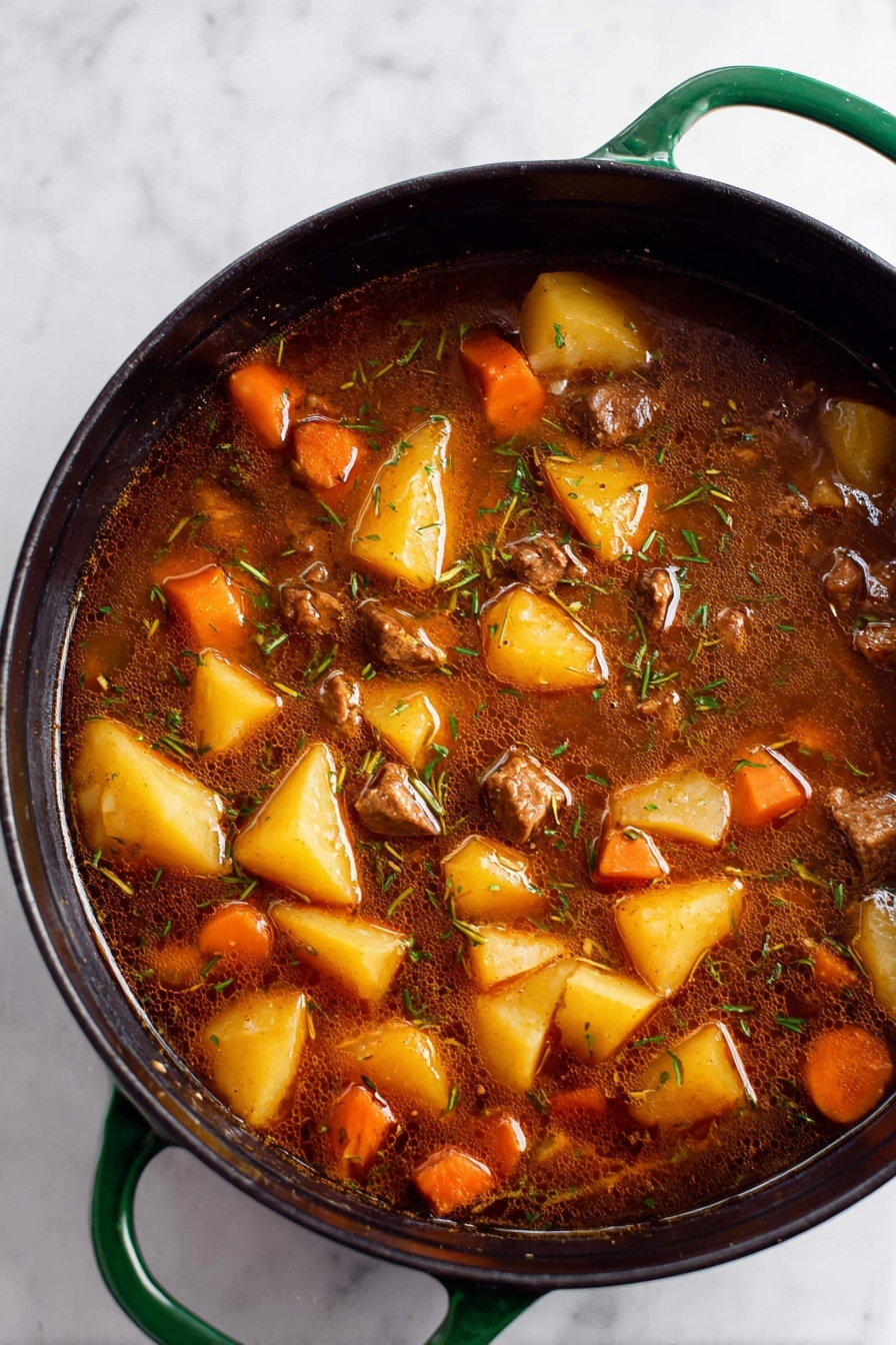 Vegan Irish Stew Gardein Beefless Tips, Vegan Irish Stew, Plant-Based Irish Stew, Vegetarian Irish Stew, Vegan Irish Stew Recipe - A close-up top view of a large black pot with green handles filled with a rich brown stew. The stew has large chunks of yellow potatoes, orange carrot pieces, and small cubes of brown meat mixed evenly throughout. The broth is dark, slightly oily, with visible thin strands of herbs floating on the surface. The pot sits on a white marbled surface. photo taken with an iphone --ar 2:3 --v 7