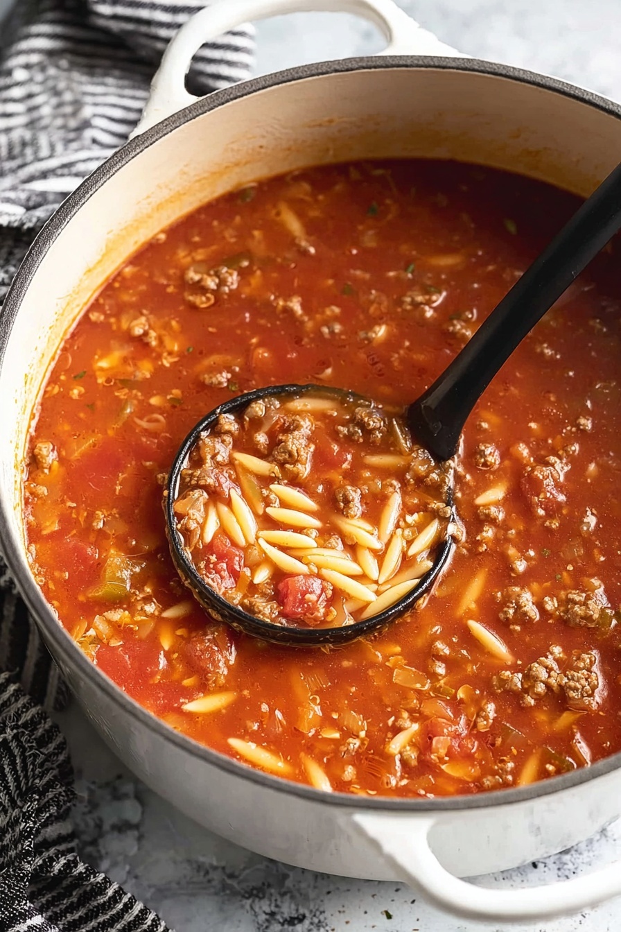 Italian Sausage Soup with Orzo, hearty sausage and orzo soup, comforting Italian sausage soup, easy sausage and orzo recipe, flavorful sausage soup - A white pot filled with a thick tomato soup that has three visible layers: a bright red tomato base with a smooth texture, mixed with small chunks of cooked ground meat in brown color, and short, oval-shaped pieces of light yellow pasta scattered throughout. A black ladle scoops some soup near the center, showing all three layers together with a shiny, moist texture. The pot is on a white marbled surface with a black-and-white striped cloth nearby. Photo taken with an iphone --ar 2:3 --v 7