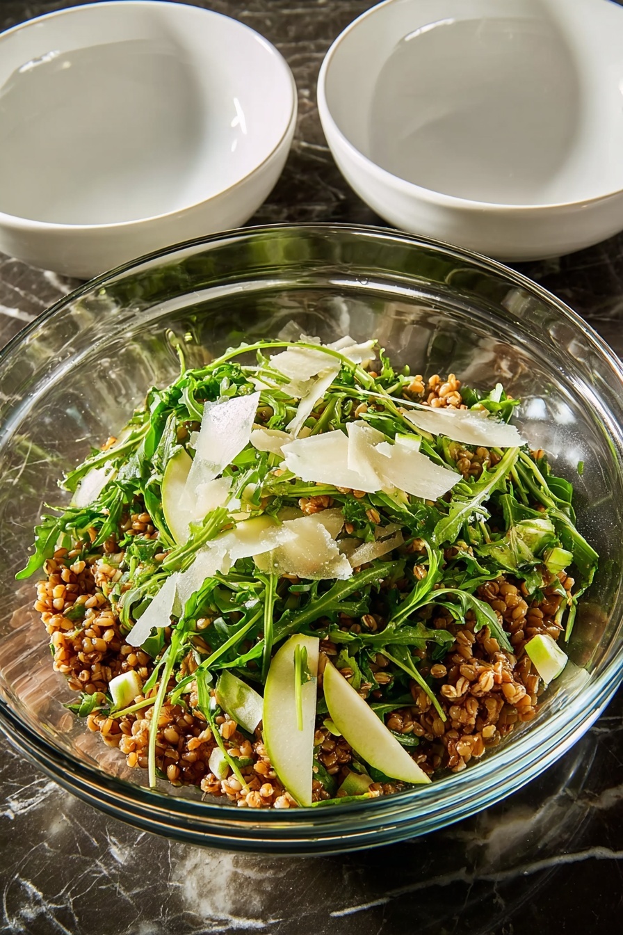Ultimate Farro Salad with Apple and Arugula, healthy farro salad, apple arugula salad recipe, hearty grain salad with fruit, quick nutritious salad - A large white round plate filled with a mixed salad that has several layers visible: the base layer is light brown cooked grains, mixed evenly with bright green arugula leaves scattered throughout. There are small, light green diced pieces of zucchini layered on top, along with thin, slightly browned slices of caramelized onions that add texture. Sprinkled lightly over the salad are thin shavings of light-colored cheese and small pieces of green herbs, giving a fresh look. The salad shows a mix of textures from soft grains to leafy greens and crunchy bits, all placed on a white marbled surface. photo taken with an iphone --ar 2:3 --v 7