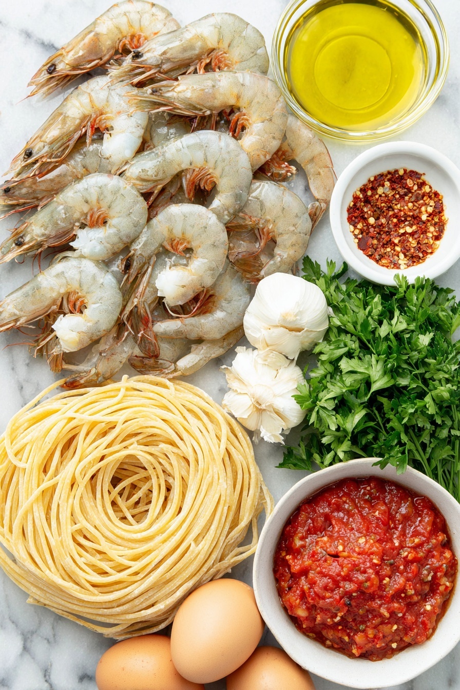 Shrimp Fra Diavolo, spicy seafood pasta, quick seafood dinner, Italian shrimp dish, flavorful shrimp recipes - Flat lay of dry linguine pasta neatly coiled, plump large shrimp with tails on arranged in a gentle curve, a small white bowl filled with shiny olive oil, a small white bowl containing bright red Calabrian chili paste, a cluster of fresh garlic cloves with papery skins intact, a small white bowl of vivid red crushed San Marzano tomatoes, fresh vibrant green parsley sprigs artistically placed, a small white bowl holding mixed red pepper flakes, and three whole uncracked brown eggs arranged symmetrically, all placed on a clean white marble surface, soft natural light, photo taken with an iPhone, professional food photography style, fresh ingredients, white ceramic bowls, no bottles, no duplicates, no utensils, no packaging --ar 2:3 --v 7 --p m7354615311229779997