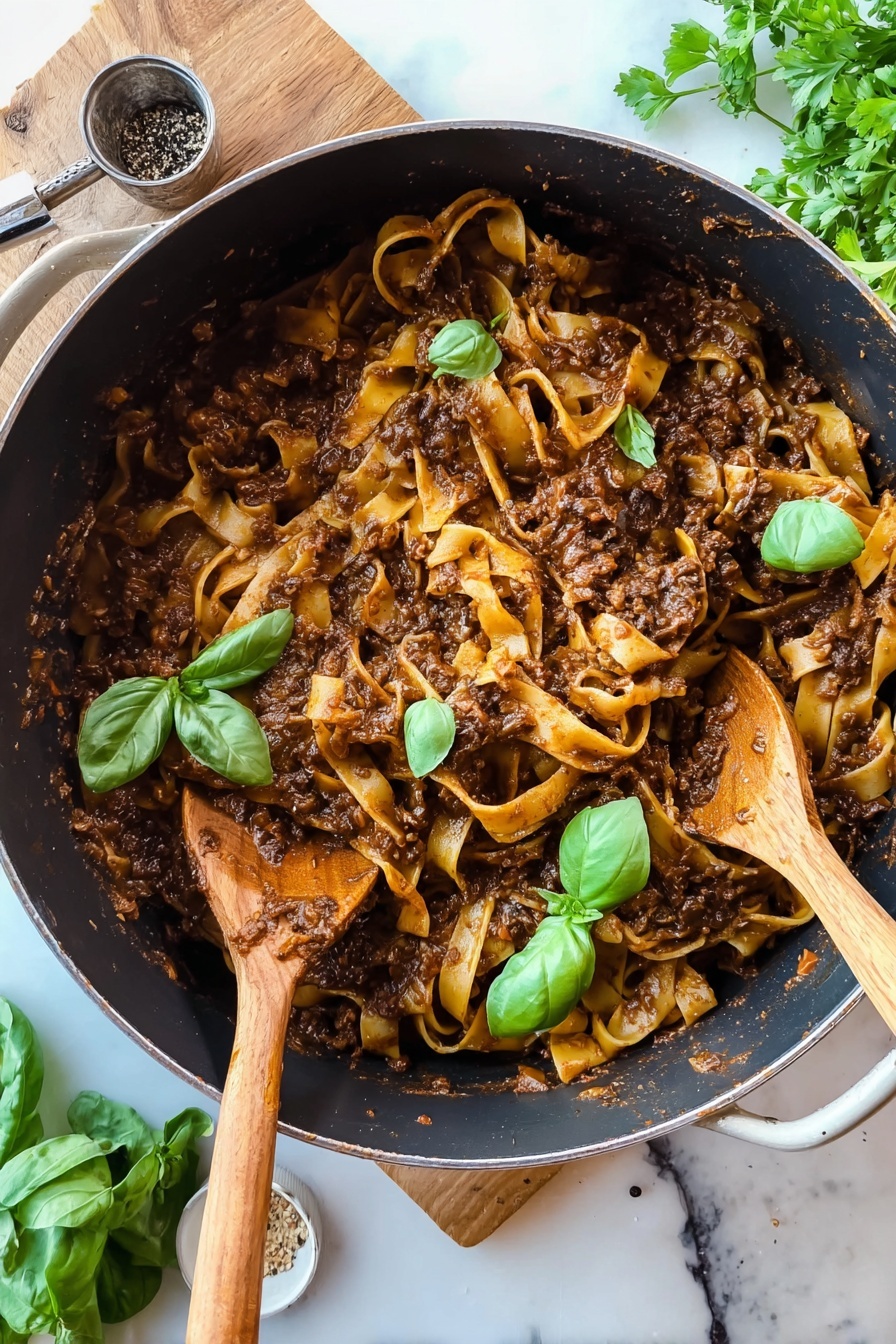 Creamy Mushroom Ragu with Pasta, mushroom pasta, hearty mushroom sauce, vegetarian pasta recipes, easy mushroom ragu - A deep black pot filled with wide, flat pasta noodles mixed with thick, dark brown meat sauce that has small bits of vegetables, topped with fresh bright green basil leaves scattered over the pasta. Two wooden spoons rest inside the pot with sauce on them, one on the left partly covered and one on the right partly submerged in the pasta. The pot sits on a wooden surface with fresh parsley and a measuring spoon with black pepper near it, all on a white marbled background. Photo taken with an iphone --ar 2:3 --v 7